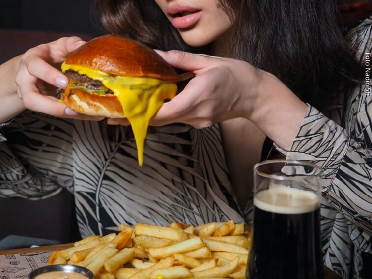 Mulher comendo fast food (hambúrguer, batata frita e refrigerante), um dos desejos causado pela fome emocional.