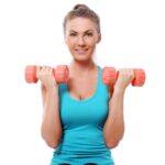 Mulher exibe músculos bíceps com dois halteres, um em cada mão.