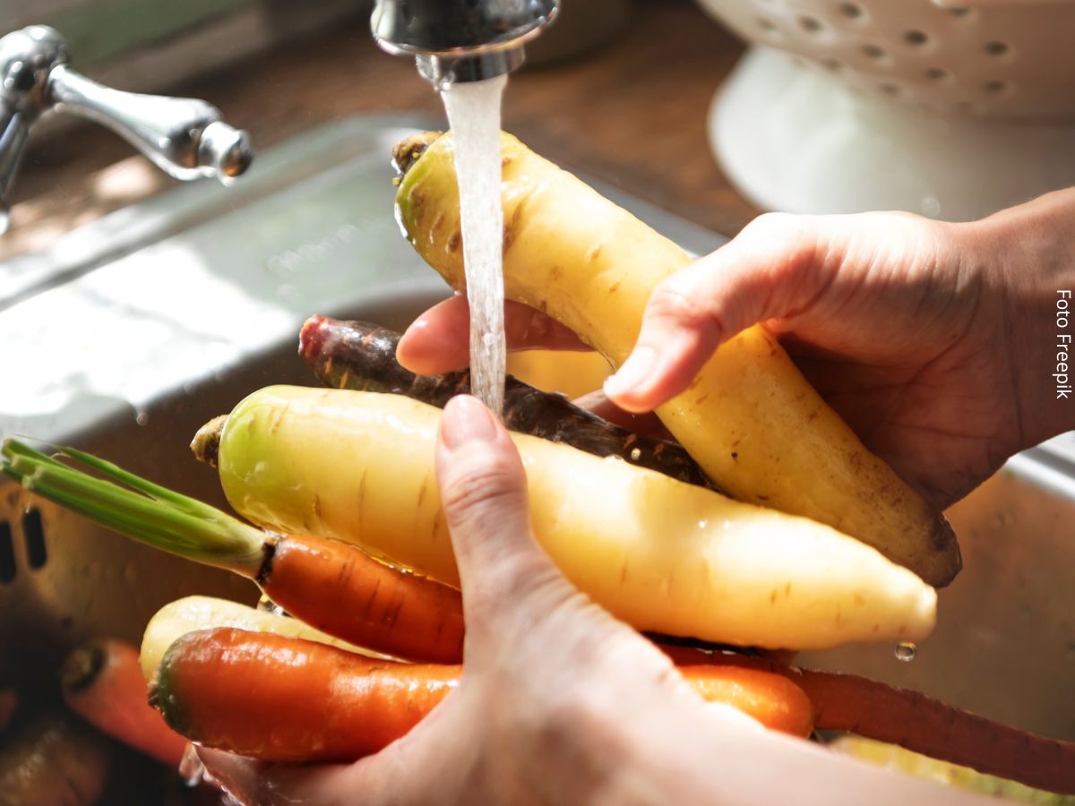 Close-up das mãos de uma mulher lavando vegetais na pia da cozinha, mostrando cuidados com os alimentos