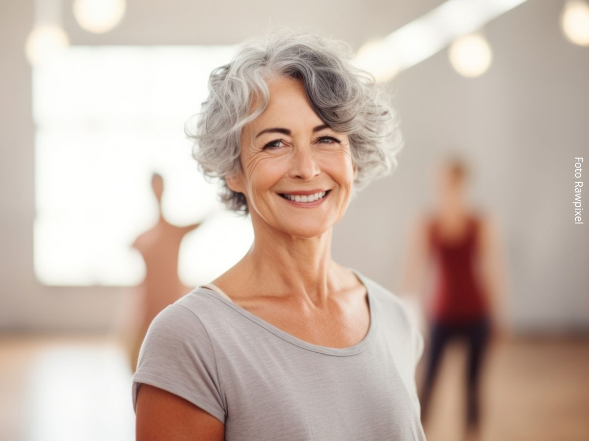Mulher de cabelos grisalhos sorrindo após uma aula de ginástica ou de dança na academia