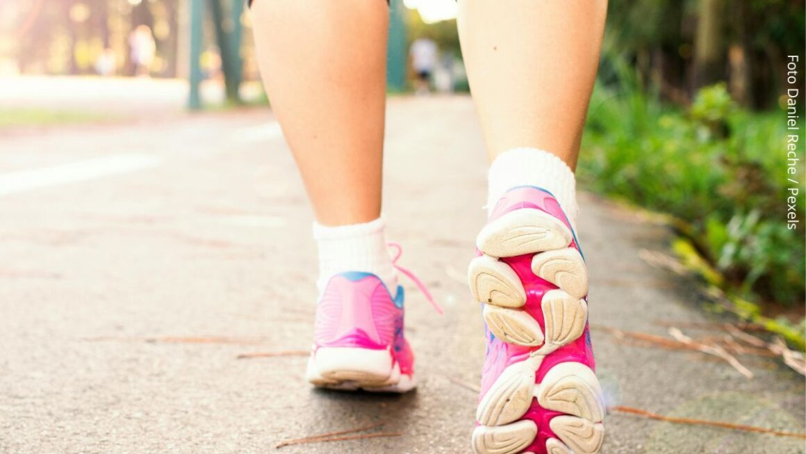 Visão por trás dos pés e de parte das pernas de uma mulher a caminhar ao ar livre para se exercitar