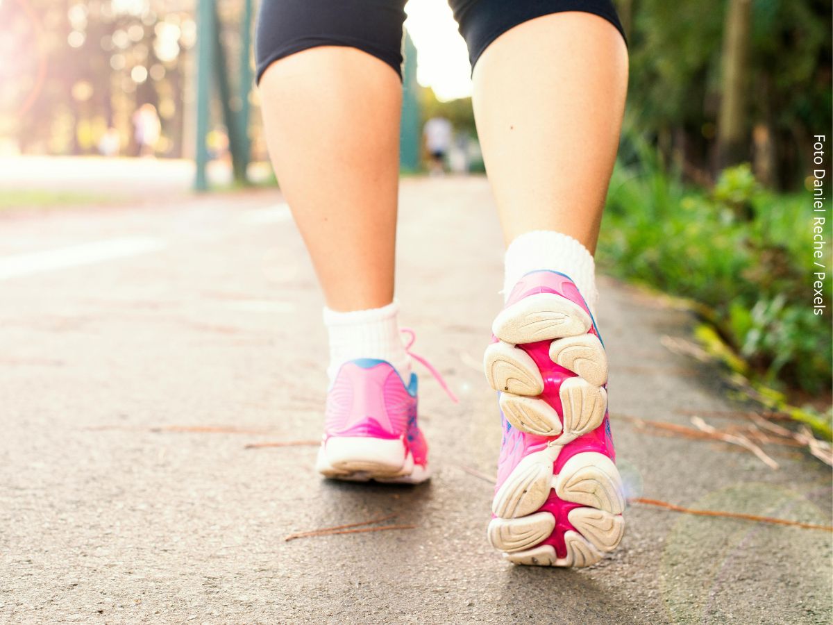 Visão por trás dos pés e de parte das pernas de uma mulher a caminhar ao ar livre para se exercitar