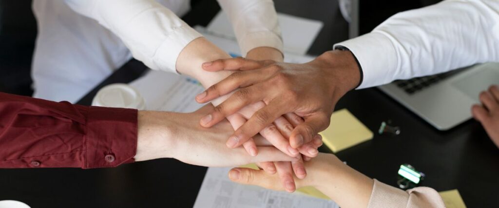 Mãos sobrepostas de funcionários tendo ao fundo a mesa do escritório. Construir relacionamentos profissionais fortes requer dedicação
