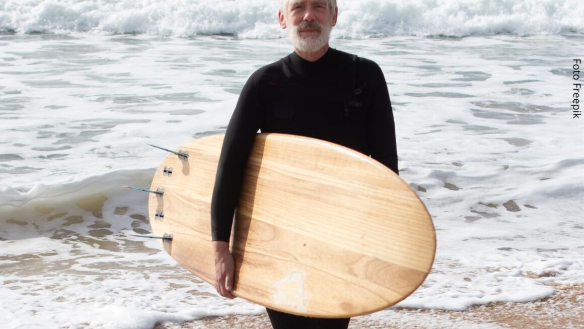 Retrato de homem maduro, de costas para o mar e com roupa de neoprene, segurando uma prancha de surf. Conceito de nunca é tarde para começar algo novo