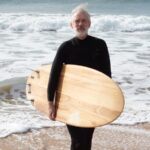 Retrato de homem maduro, de costas para o mar e com roupa de neoprene, segurando uma prancha de surf. Conceito de nunca é tarde para começar algo novo