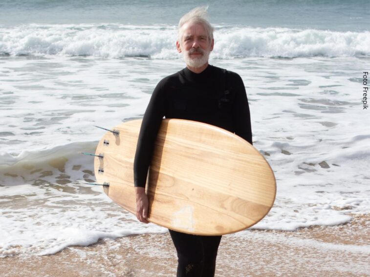 Retrato de homem maduro, de costas para o mar e com roupa de neoprene, segurando uma prancha de surf. Conceito de nunca é tarde para começar algo novo