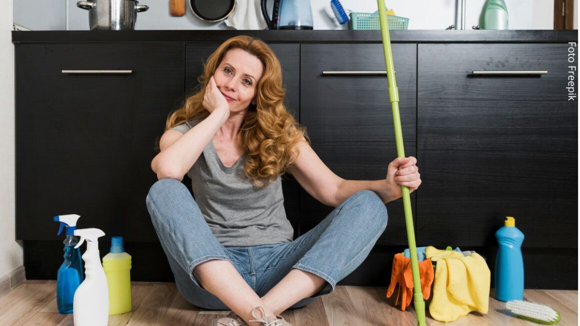 Vista frontal de mulher sentada no chão, segurando o esfregão com produtos de limpeza ao lado. Ideia de não divisão de tarefas domésticas