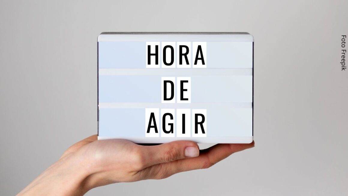 Imagem de uma mão feminina segurando uma claquete com a frase hora de agir.