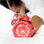 Close-up de um despertador sendo desligado por uma mulher jovem sonolenta deitada na cama. Conceito de um tipo de sono