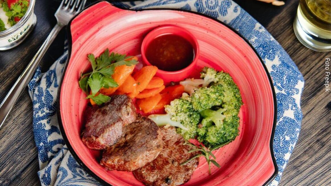 Close-up de um prato com carne grelhada, brócolis, feijão e vegetais, compondo a ideia de alimentos saudáveis.