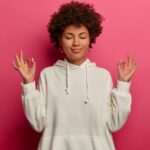 Mulher negra jovem com as duas mãos erguidas na altura do ombro meditando, em busca de como ter paciência