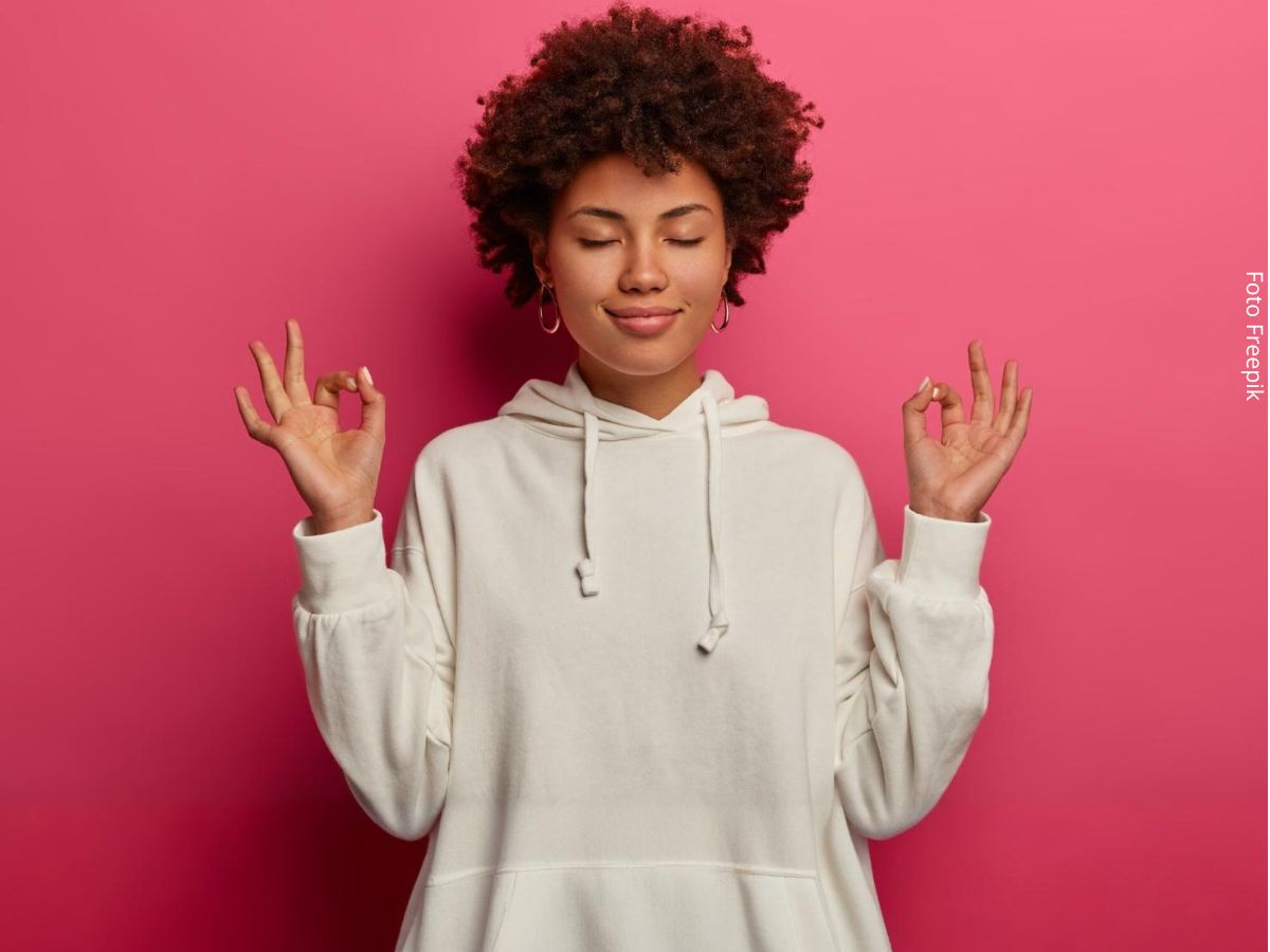 Mulher negra jovem com as duas mãos erguidas na altura do ombro meditando, em busca de como ter paciência
