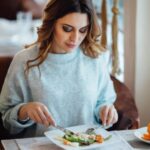 Imagem de mulher branca, bonita, sentada à mesa mostrando como usar os talheres com etiqueta e naturalidade, com garfo na mão esquerda e faca na mão direita.