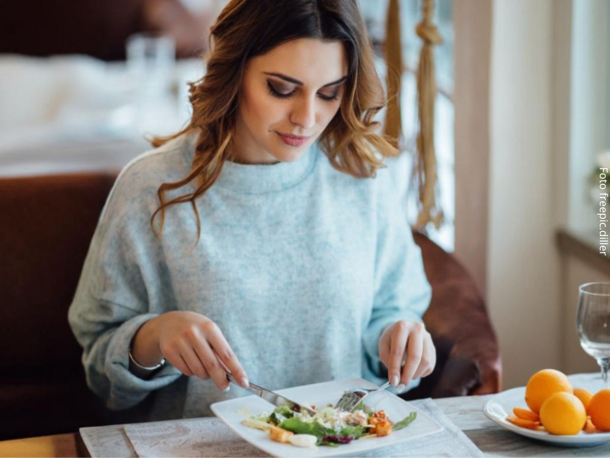 Imagem de mulher branca, bonita, sentada à mesa mostrando como usar os talheres com etiqueta e naturalidade, com garfo na mão esquerda e faca na mão direita.