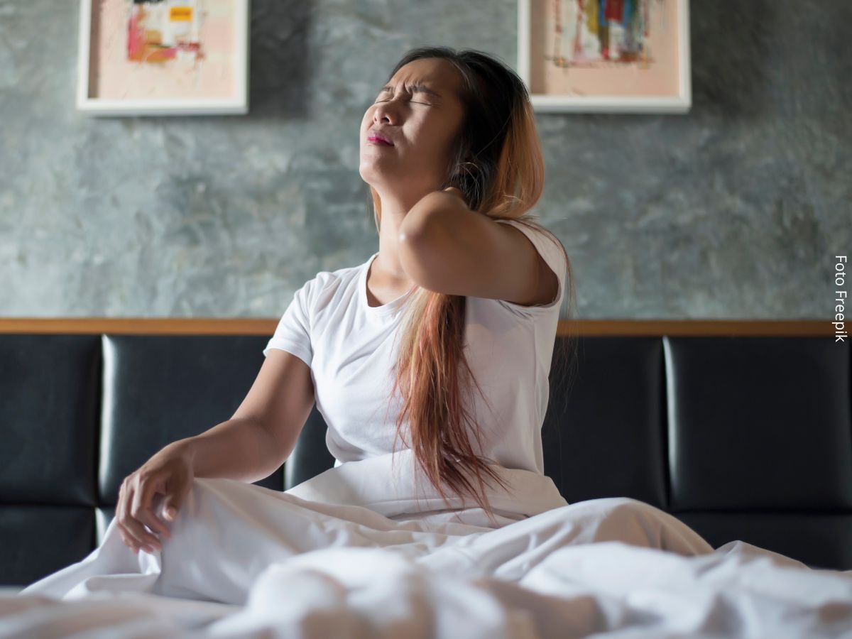 Close-up de mulher jovem sentada na cama com dor no pescoço e corpo cansado depois de acordar