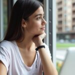 Imagem de uma mulher jovem olhando pela janela distraída diante de um laptop aberto, aparentando falta de concentração