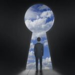 Imagem de um homem em pé de costas olhando para o céu azul por uma enorme fechadura, simbolizando um um mundo de possibilidades que uma mentalidade empreendedora oferece.