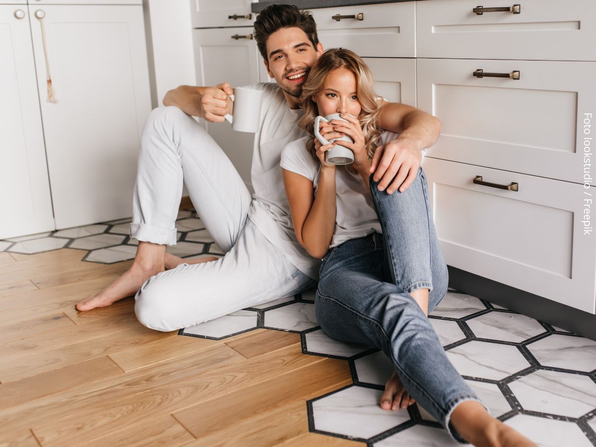 Casal feliz sentado no chão da cozinha com uma xicara de café na mão, desfrutando de morar junto