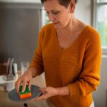 Imagem de uma mulher madura lavando a louça com uma esponja em bom estado de uso, garantindo a segurança alimentar e a higiene da cozinha