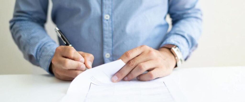 Close-up das mãos de um homem segurando uma caneta assinando documentos