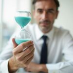 Imagem de homem de terno segurando uma ampulheta, sugerindo as escolhas da vida: mais tempo ou mais dinheiro.