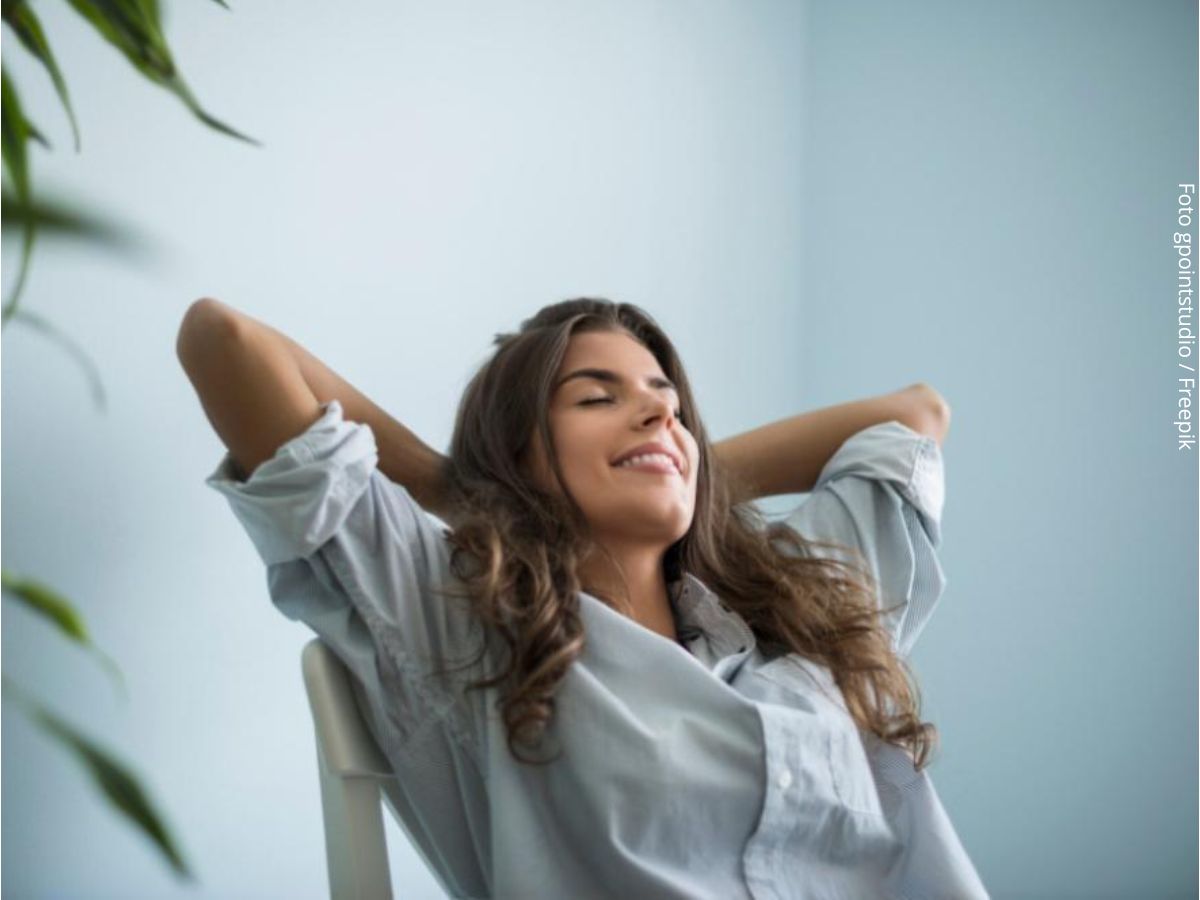 Imagem de mulher jovem sentada sorrindo com as mãos na nuca, com ar de felicidade