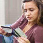 Close-up de uma mulher segurando cartões de crédito, indecisa sobre qual escolher para fazer seus gastos