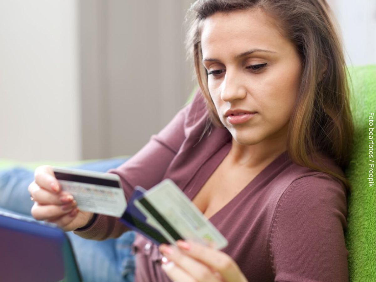 Close-up de uma mulher segurando cartões de crédito, indecisa sobre qual escolher para fazer seus gastos