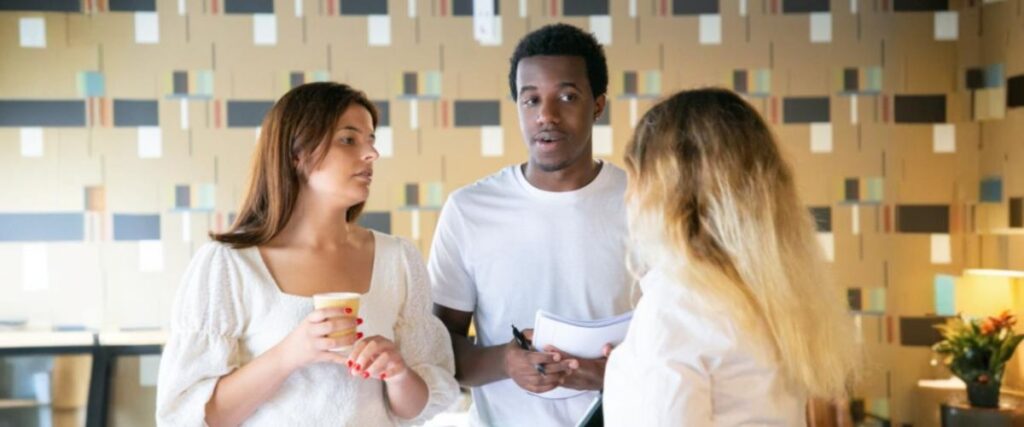 Imagem de um homem negro e duas mulheres brancas conversando no escritório.