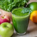 Imagem de copo de suco verde sobre a mesa, com maçãs verde e vermelha ao lado, exemplificando alimentos anti-inflamatórios