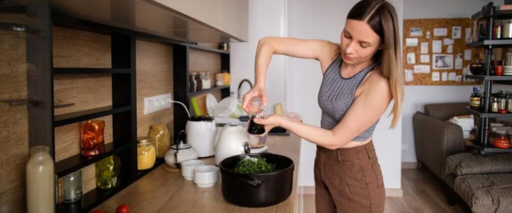 Imagem de uma mulher jovem na cozinha preparando o  almoço.