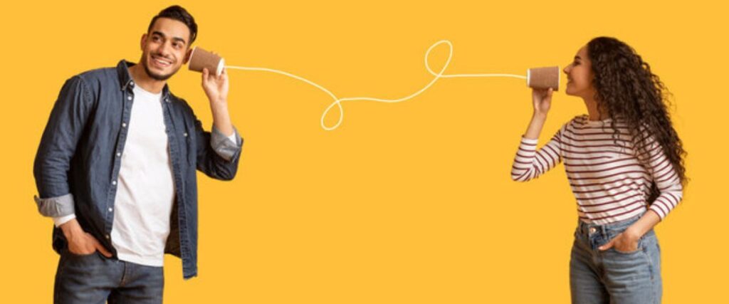 Imagem de casal simulando comunicação através de telefone de lata sobre fundo amarelo