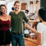 Imagem mostra convidada entregando garrafa de vinho de presente para anfitrião