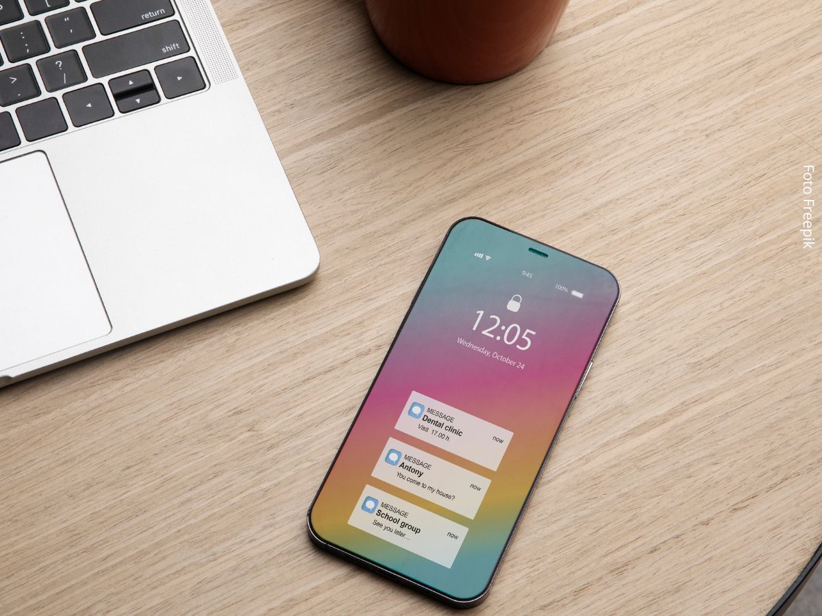 Vista de um smartphone sobre a mesa, ao lado de um laptop e uma xícara de café, com mensagens na tela inicial esperando ser respondidas com base nas regras de etiqueta no WhatsApp