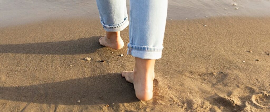 Imagem vista de trás de pés femininos caminhando na areia.