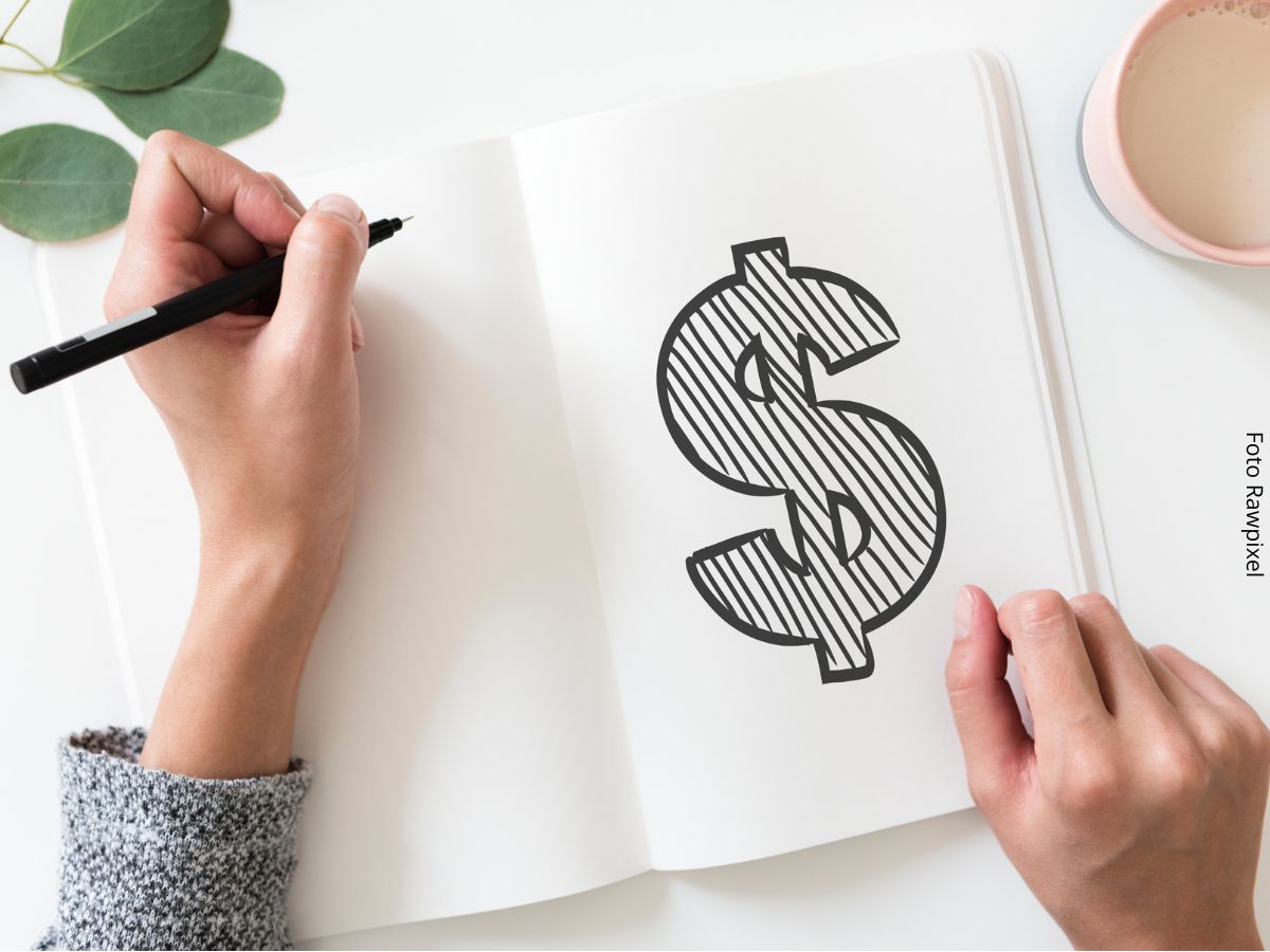 Close-up de uma pessoa desenhando o símbolo do cifrão num caderno, simbolizando a independência financeira