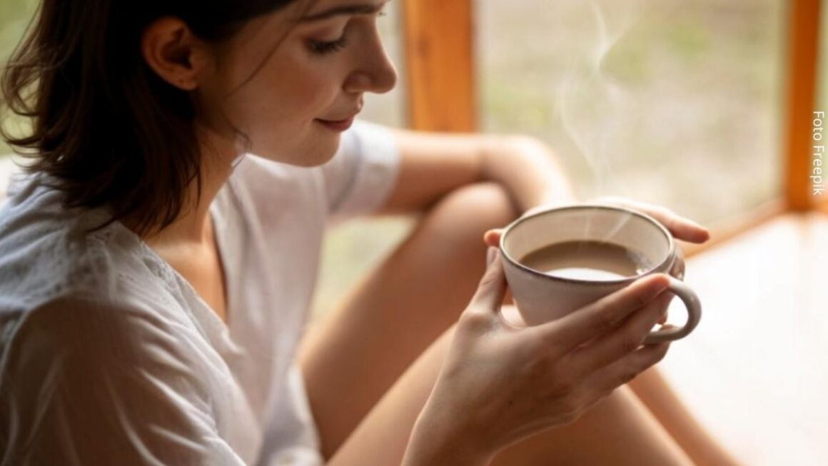 Imagem de uma mulher jovem sentada no chão relaxada, segurando uma xícara de café, sugerindo presença.