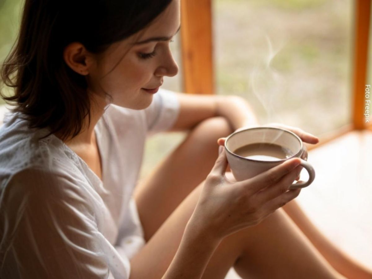 Imagem de uma mulher jovem sentada no chão relaxada, segurando uma xícara de café, sugerindo presença.