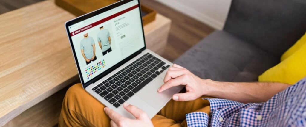 Imagem de um homem no computador trabalhando na sua loja de roupa de impressão sob demanda.