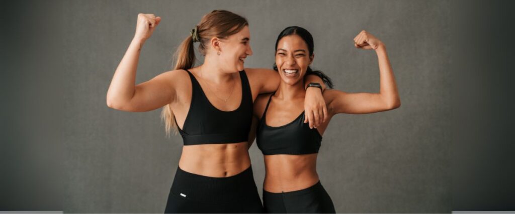 Imagem de duas mulheres jovens exibindo os bíceps e sorrindo