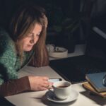 Imagem de uma mulher olhando o celular distraída, a repetir hábitos comuns da procrastinação.