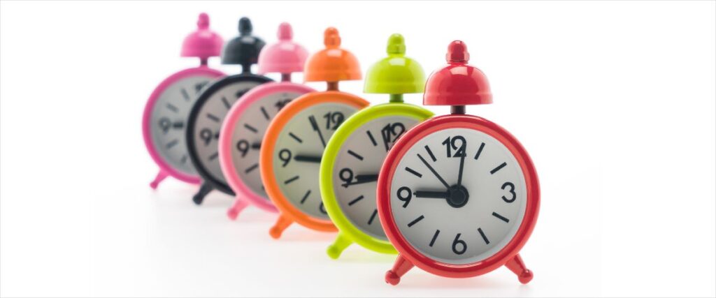 Imagem de relógios despertadores coloridos em sequência marcando a mesma hora.