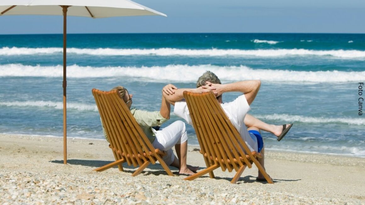 Imagem de um casal relaxado em suas cadeiras na areia da praia apreciando o mar graças à renda da aposentadoria oriunda de investimentos como o Tesouro Renda+