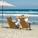 Imagem de um casal relaxado em suas cadeiras na areia da praia apreciando o mar graças à renda da aposentadoria oriunda de investimentos como o Tesouro Renda+