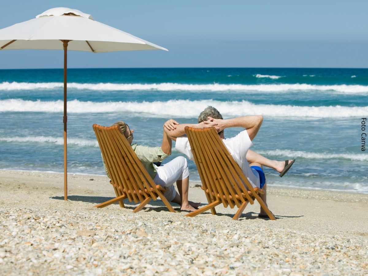 Imagem de um casal relaxado em suas cadeiras na areia da praia apreciando o mar graças à renda da aposentadoria oriunda de investimentos como o Tesouro Renda+