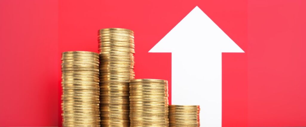 Imagem de moedas empilhadas à frente de um fundo vermelho e o desenho de uma seta apontada para cima.