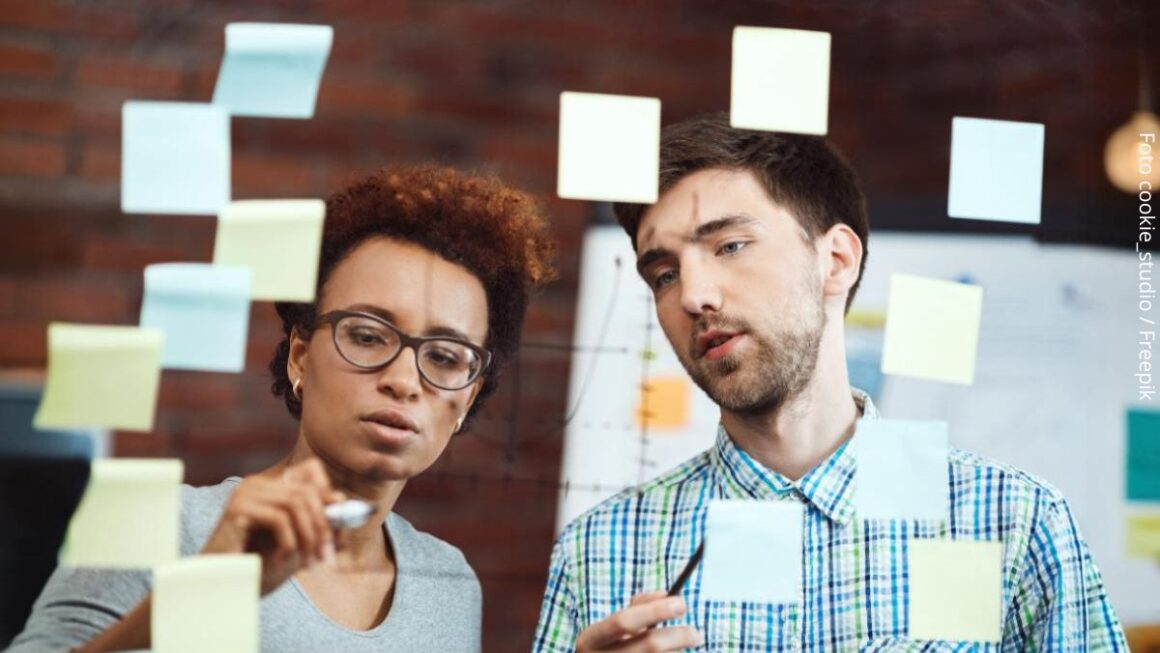 Imagem de dois líderes - uma jovem negra e um rapaz branco - no escritório, elaborando estratégias para se antecipar a problemas, exemplificando a ideia do que é ser proativo