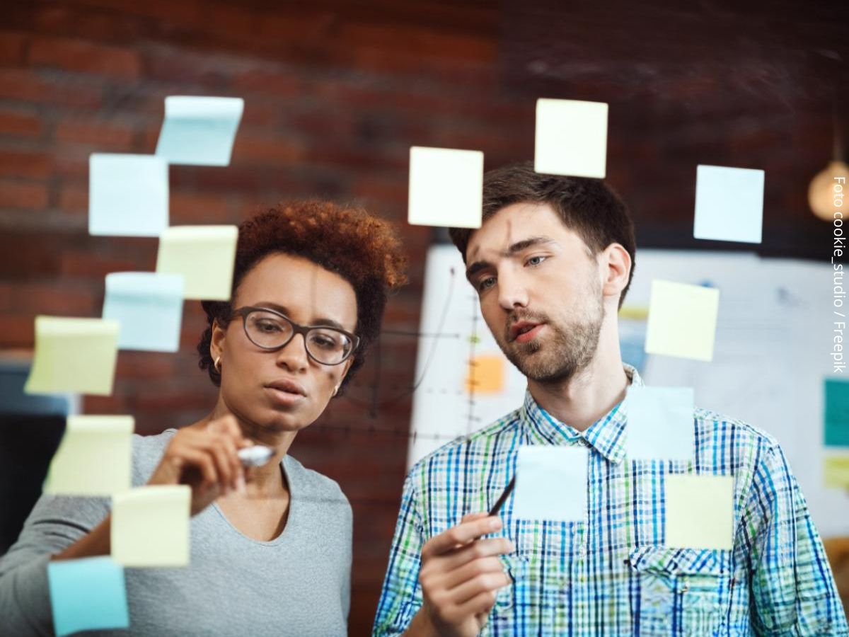 Imagem de dois líderes - uma jovem negra e um rapaz branco - no escritório, elaborando estratégias para se antecipar a problemas, exemplificando a ideia do que é ser proativo