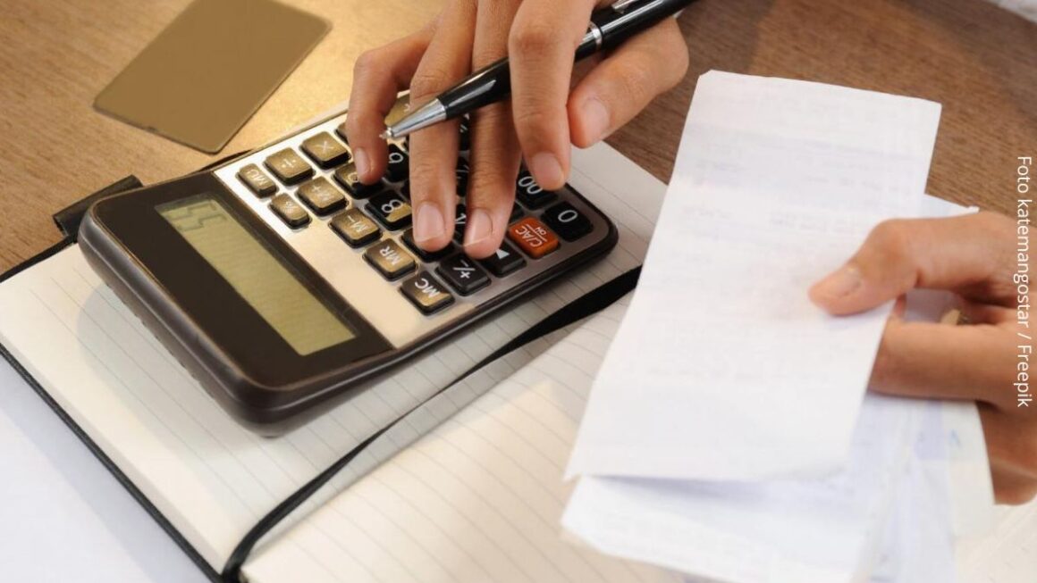 Close-up de pessoa segurando notas e fazendo contas numa calculadora, tentando se organizar para sair de dívidas.