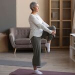 Imagem de uma mulher madura em pé sobre uma perna fazendo exercício de equilíbrio em casa.